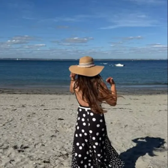 Candice sur une plage, en robe à pois et chapeau de paille